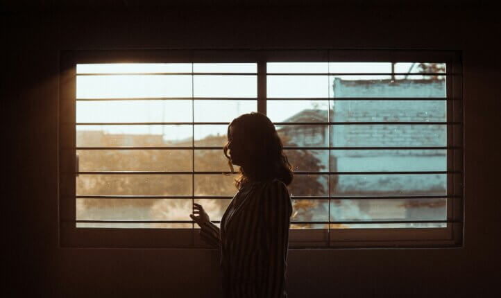 A woman standing by a window. Accompanies a coaching article about reslience and adaptation.